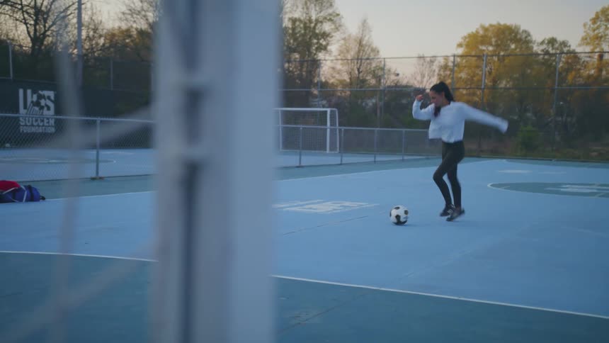 A teenage girl kicks soccer balls in to a goal