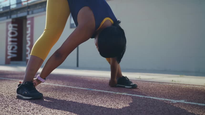 Young fit woman stretches while standing on a running track at morning