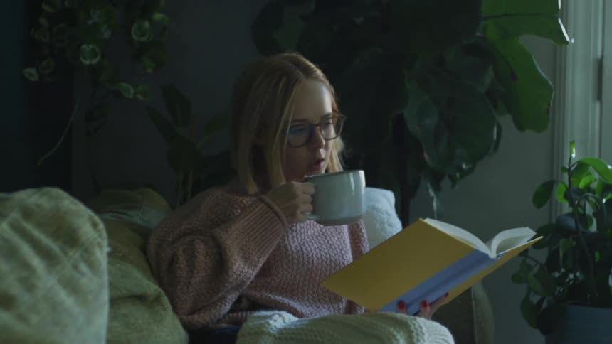 A woman drinking a cup of tea and reading a book