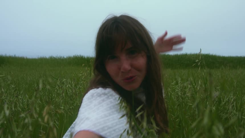 A woman playing in a grassy field with the sky and clouds in the background
