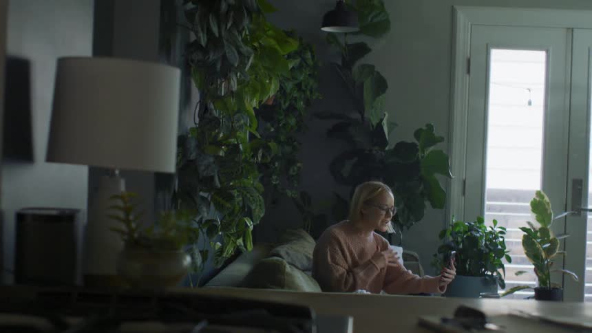 A woman in a room with glasses sitting on a couch talking on a smart phone