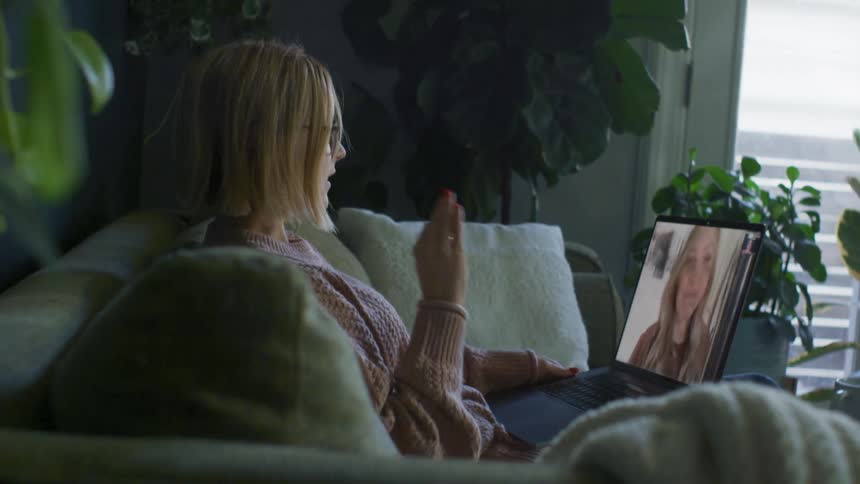 A woman in a room with glasses sitting on a couch using a laptop