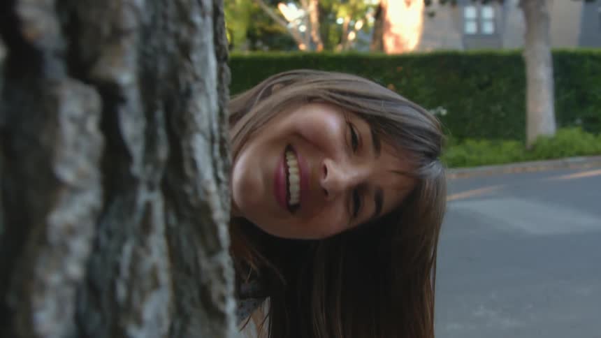A portrait of a woman leaning out from behind a tree