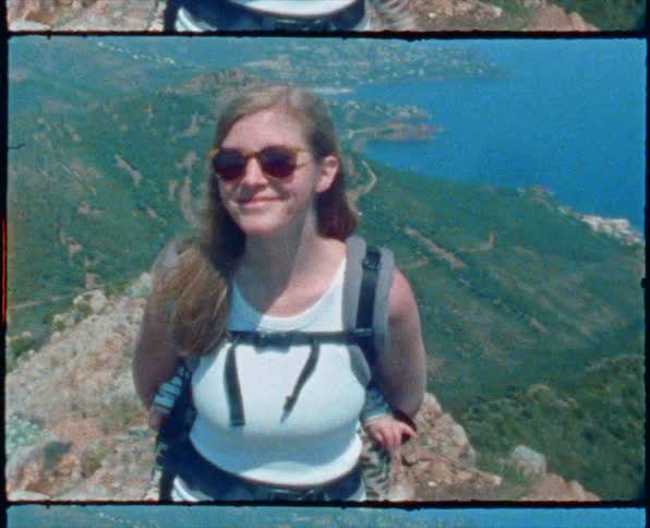A woman with her baby in a backpack carrier smiles and twirls on a ridge overlooking the ocean