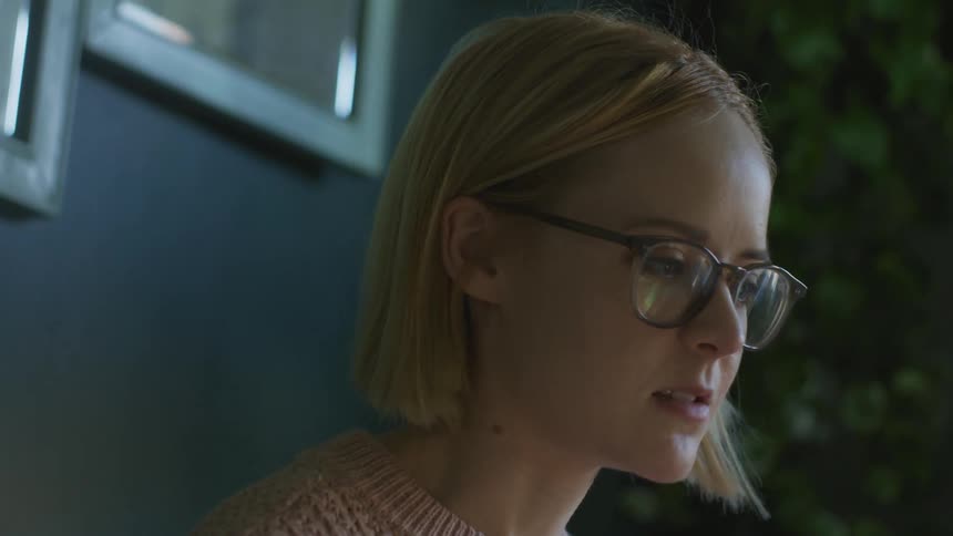 Blonde woman wearing glasses talks while she is outside near the trees