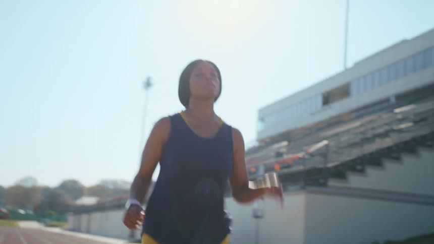 Woman running along track past stadium seating stops