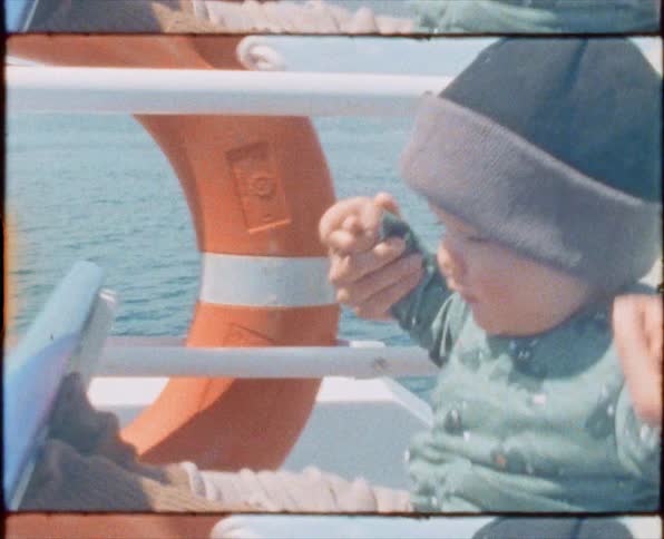 A woman and a baby on a boat with land water the sky and clouds in the background
