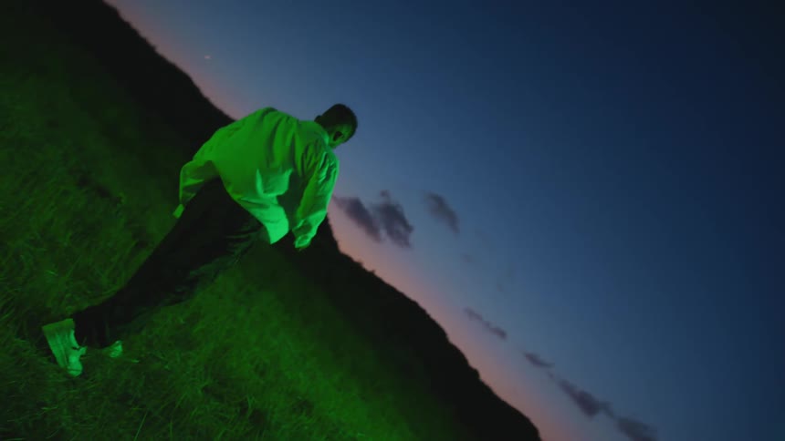 A man wearing a green shirt and sneakers stumbles through the grass