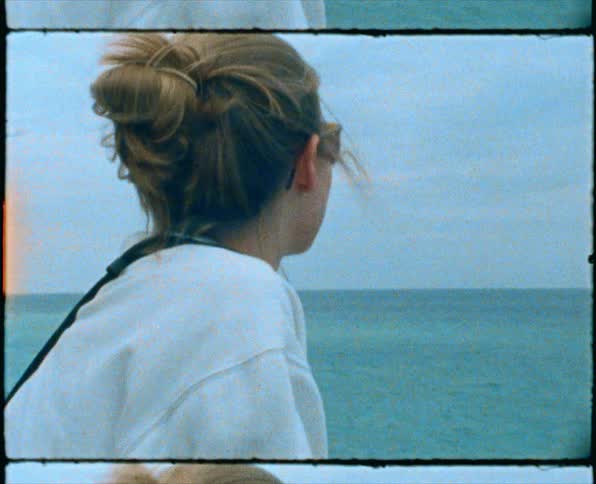 Woman wearing sweatshirt and sunglasses leans against rail looking out to sea on windy day