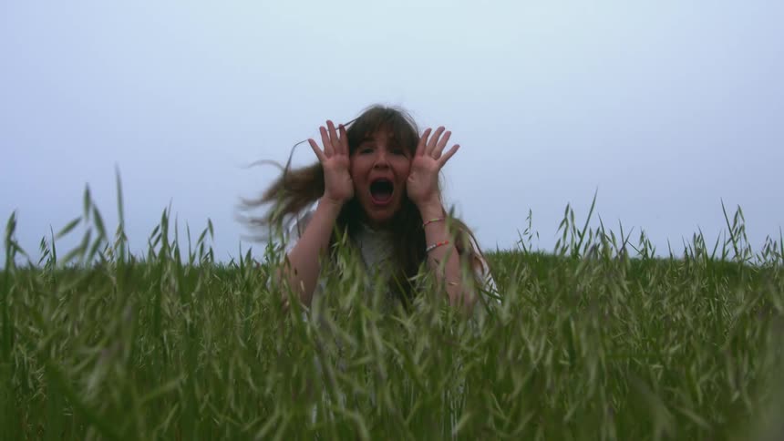 A woman plays peekaboo in the tall green grass of a large field
