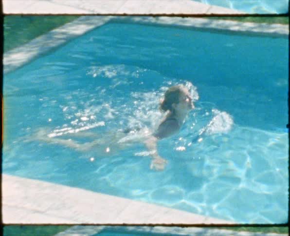 Blonde woman in bikini swims in swimming pool in garden