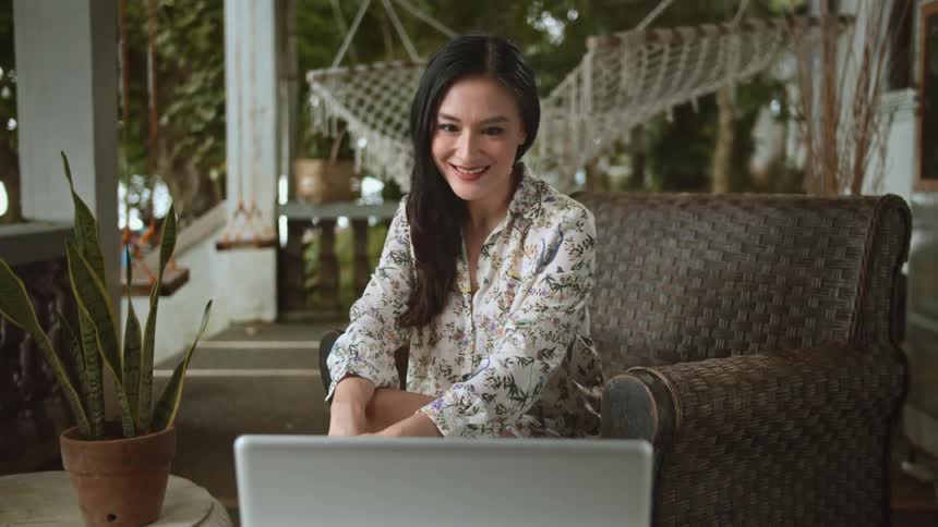 A woman having a video meeting on her laptop smiles before suddenly her expression changes