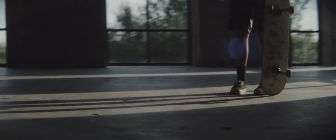 Male holds a skateboard as he stands in the middle of a large room