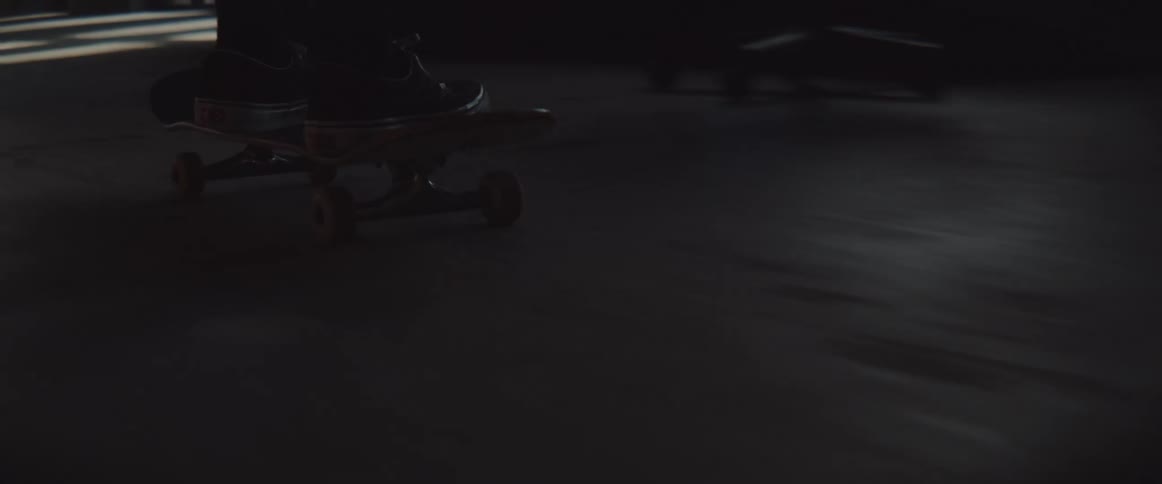 Skateboarder rides a skateboard inside a building while the sun shines in through the windows