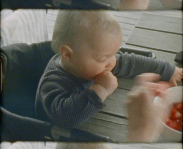 Baby sitting at the table eating sliced strawberries from a bowl