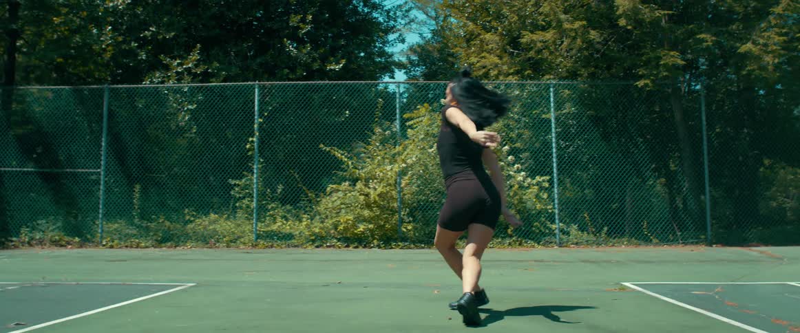A female dancer performs a series of skillful moves while atop an outdoor tennis court