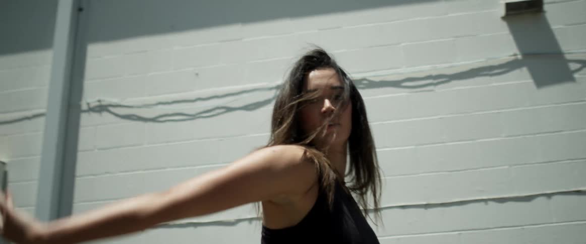 A woman dancing with a building the sky and clouds in the background