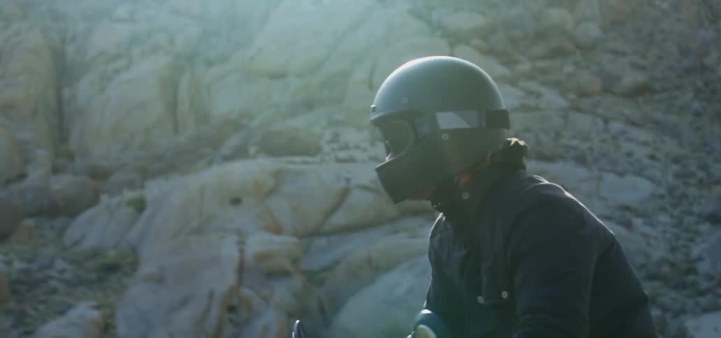 A person rides a motorcycle carefully beside a large mountain