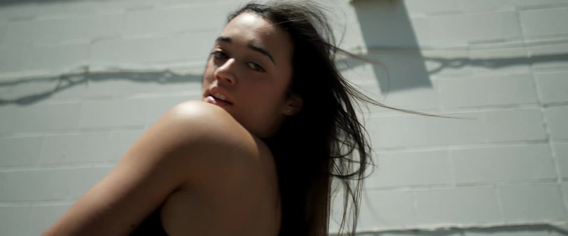 Young fit woman energetically dancing in front of a white brick wall at daytime