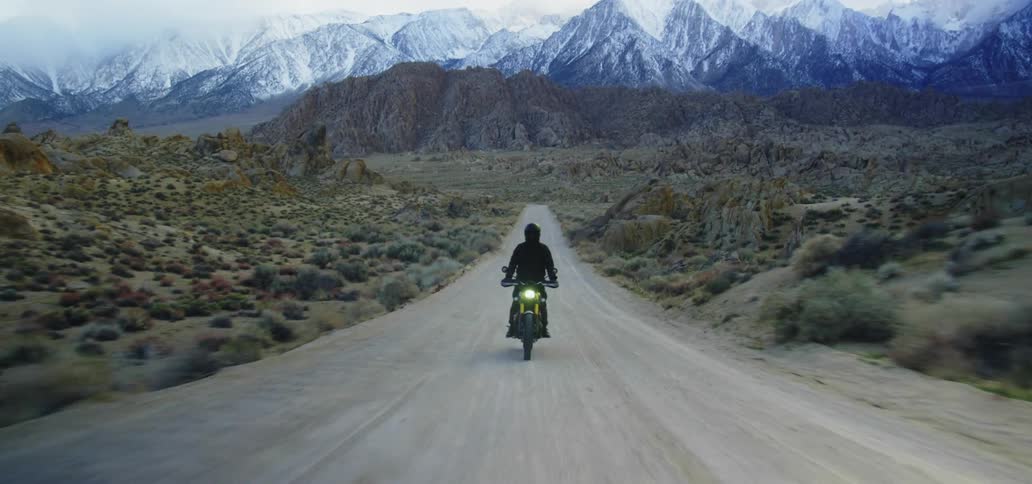 Motorcycle with headlight on is traveling fast on a road with snow covered mountains in distance