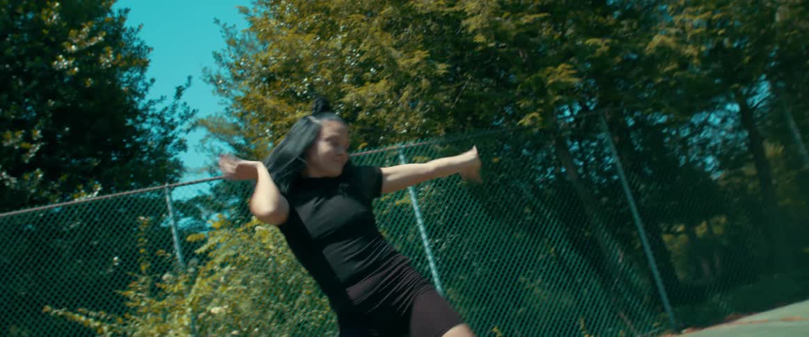 A woman dancing with a fence trees the sky and clouds in the background
