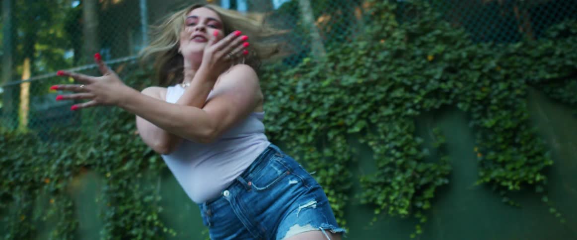 Young voluptuous woman energetically dancing near the wire fence on a park at daytime