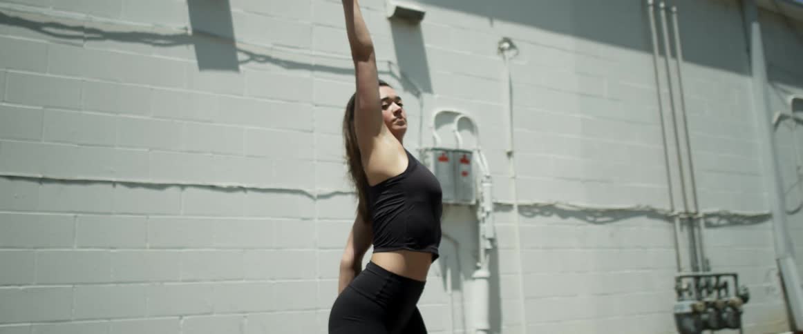 Woman dances at back of building near meters and utility connections