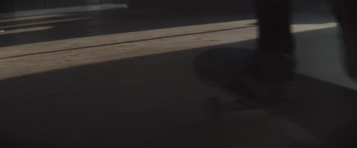 A person pushes off to roll on the skateboard inside a building on a floor covered with dirt