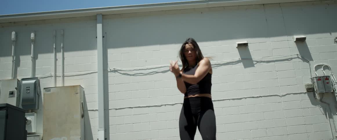 A woman dances behind a building near power meters