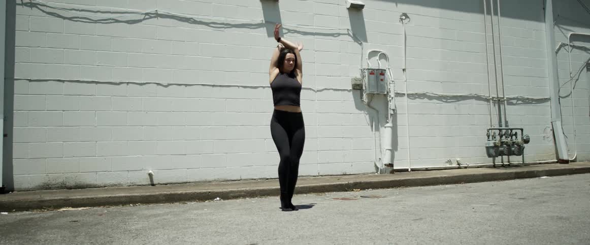 Young fit woman energetically dancing in front of a white brick wall at daytime