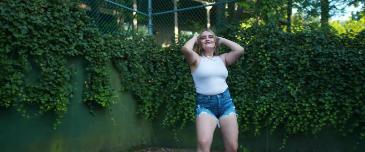 An exuberant young woman dances near a fence while outdoors