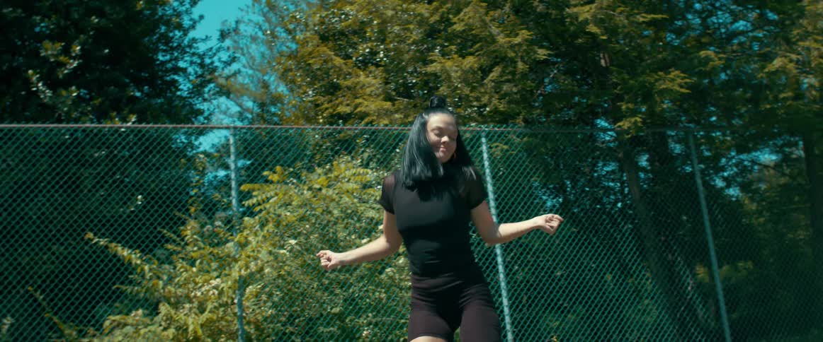 A young woman performs a choreographed dance while outdoors near a chain linked fence
