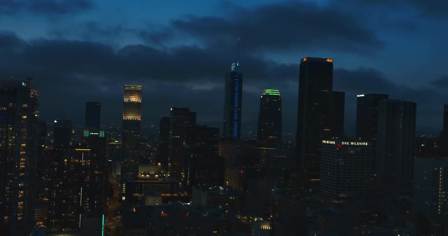 City lights and building signs shine from downtown skyscrapers under cloudy sky