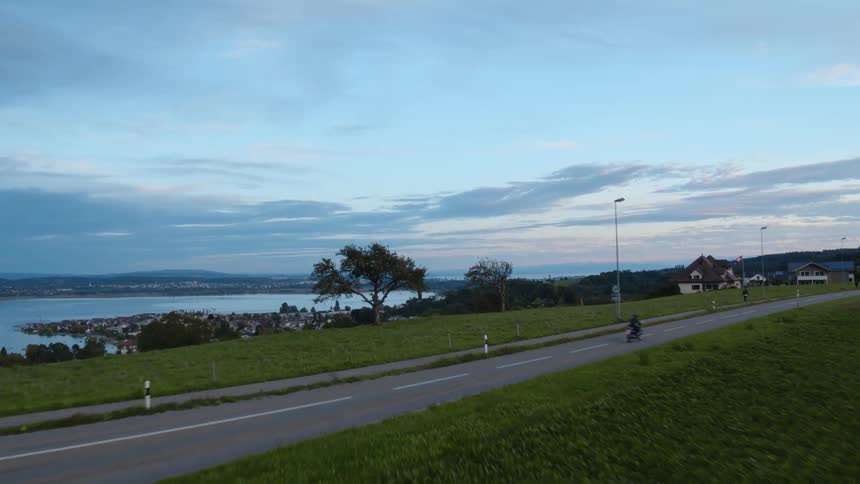 A person riding a motorcycle on a road with trees the sky and clouds in the background