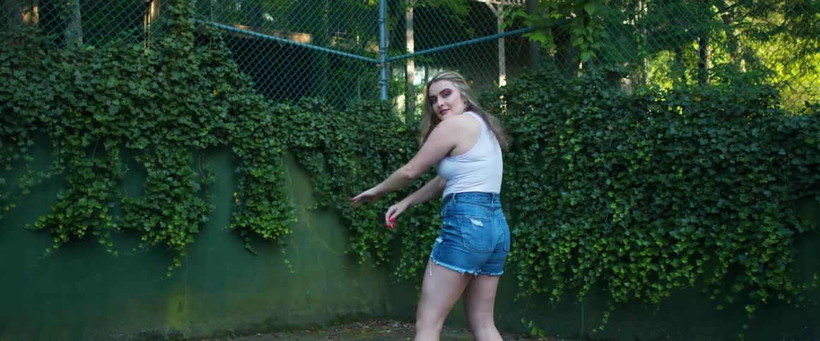 A woman does interpretive dance in a courtyard surrounded by an ivy covered fence