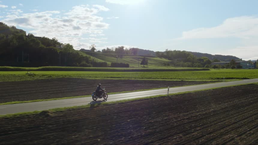 A man rides his motorcycle past farm fields
