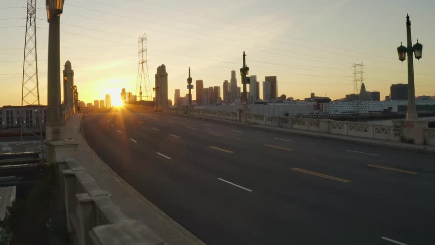 Empty bridge leading towards setting sun in pink sky backlighting the city skyline and turning skyscrapers into silhouette