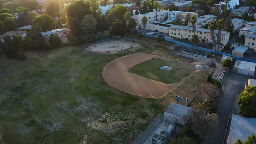 A baseball field surrounded by buildings and trees with sunlight in the background