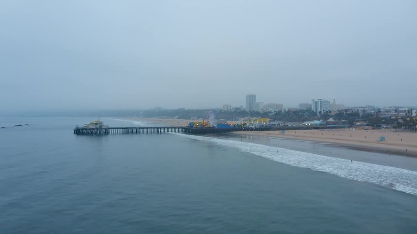 A boardwalk on the beach with an amusement park with buildings the sky and clouds in the background