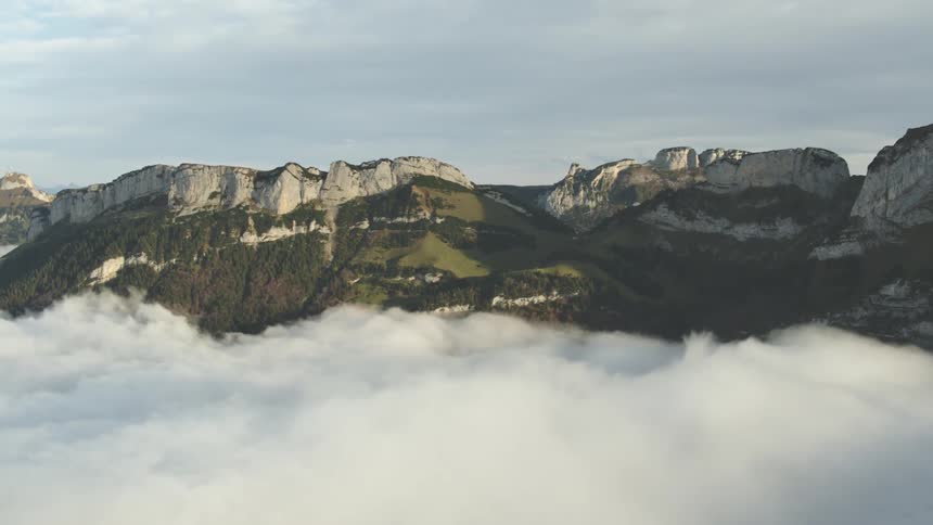 Dense fog covers lower part of forest covering cliff faces of mountains