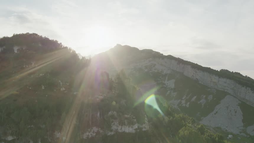 A mountain range with trees with the sun the sky and clouds in the background