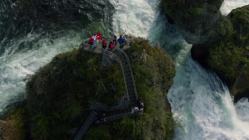 Tourists stand on steps and a platform overlooking rushing water