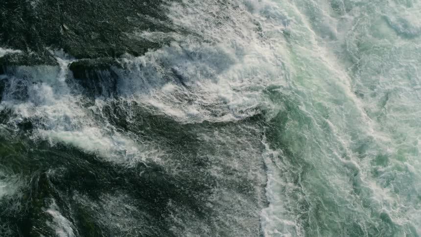 The river water flows over the rocks and splashes against a small land mass