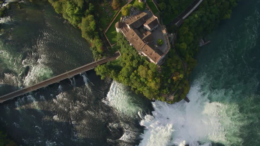 The river flows roughly over the rocks into the water below while a building sits in the forest nearby