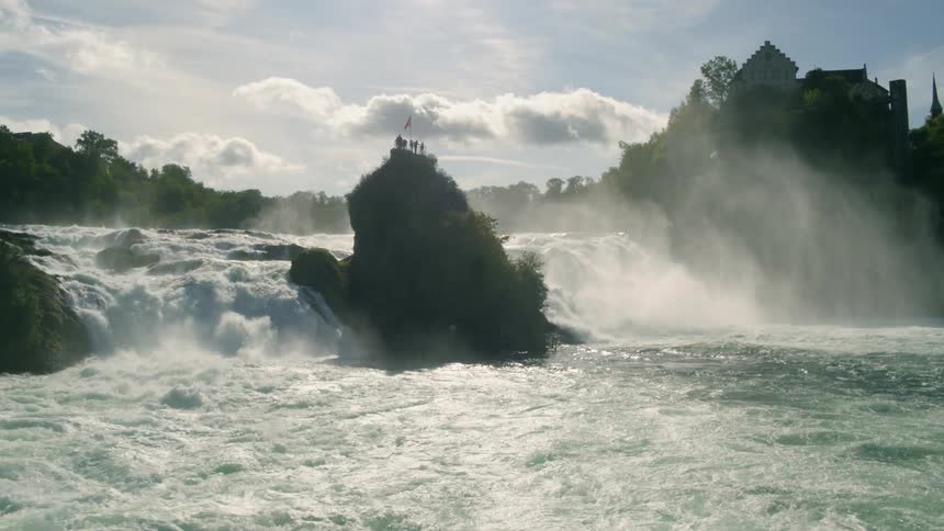 Group of people stand on a large rock in the middle of the river as the water rushes past it