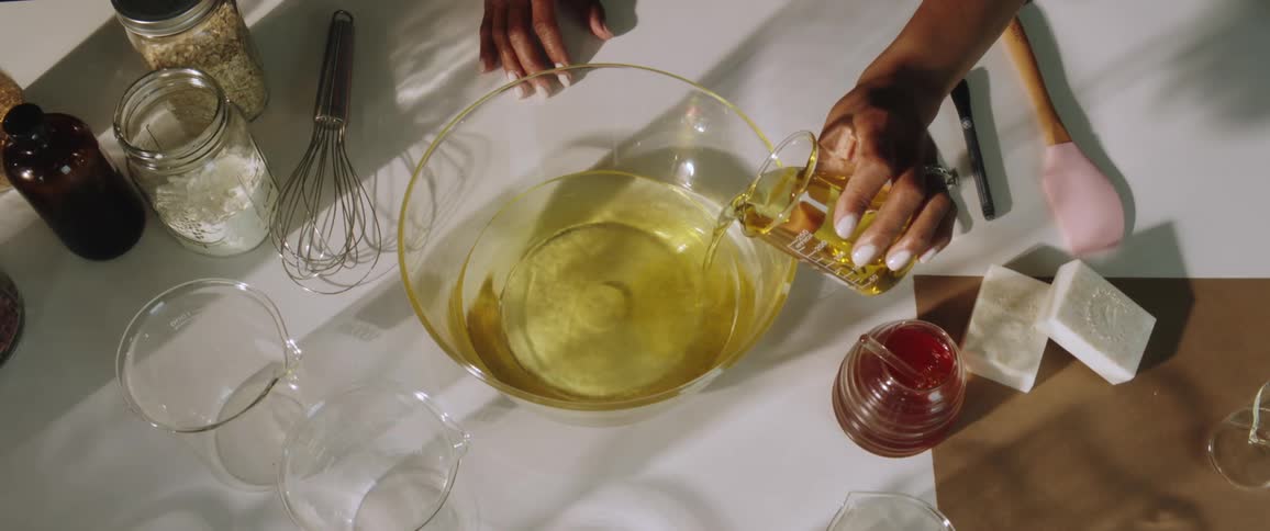 A woman in a room pouring a liquid into a mixing bowl on a table