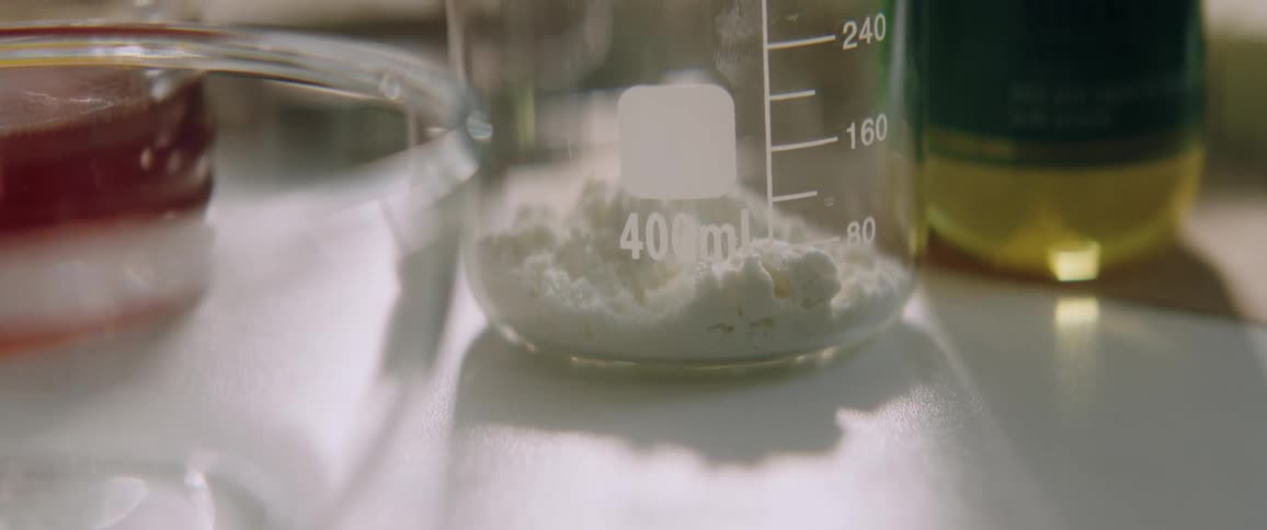 A beaker filled with white powder sits on a table next to a glass bowl