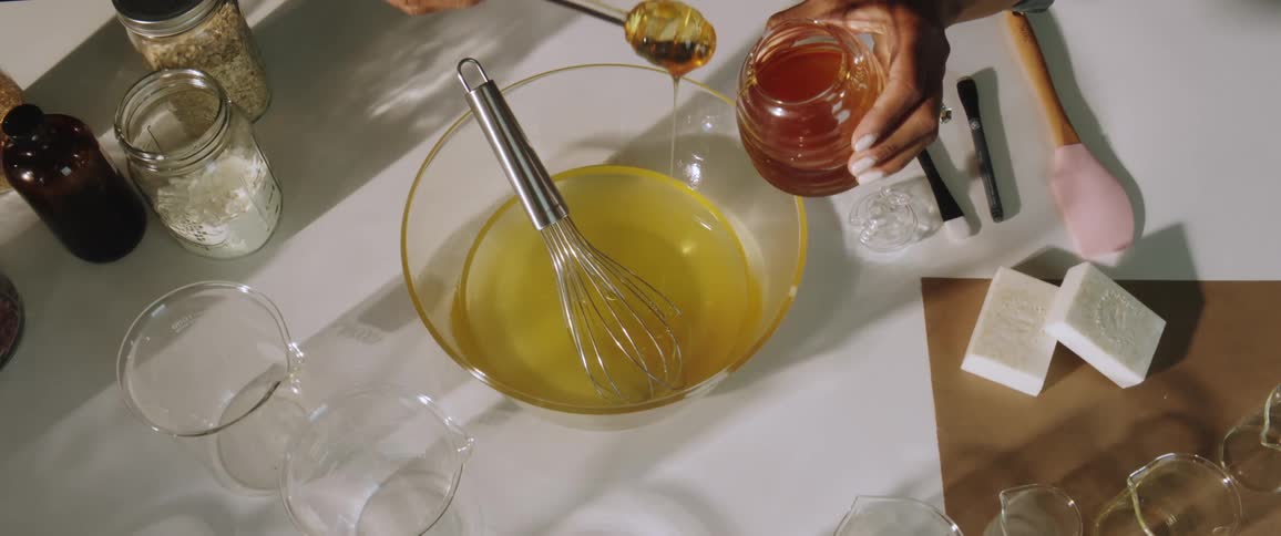 Woman adds honey to mixture in bowl while making soap