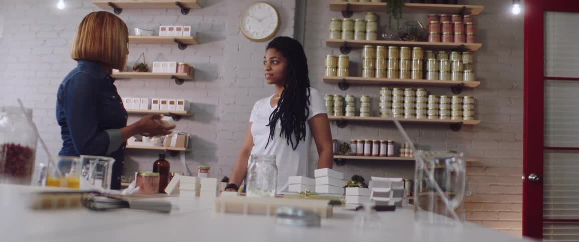 One woman talks with another woman standing in a store and holding a piece of product