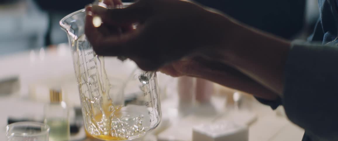 A woman drizzles honey into a large glass beaker then replaces the dipper into a honey jar